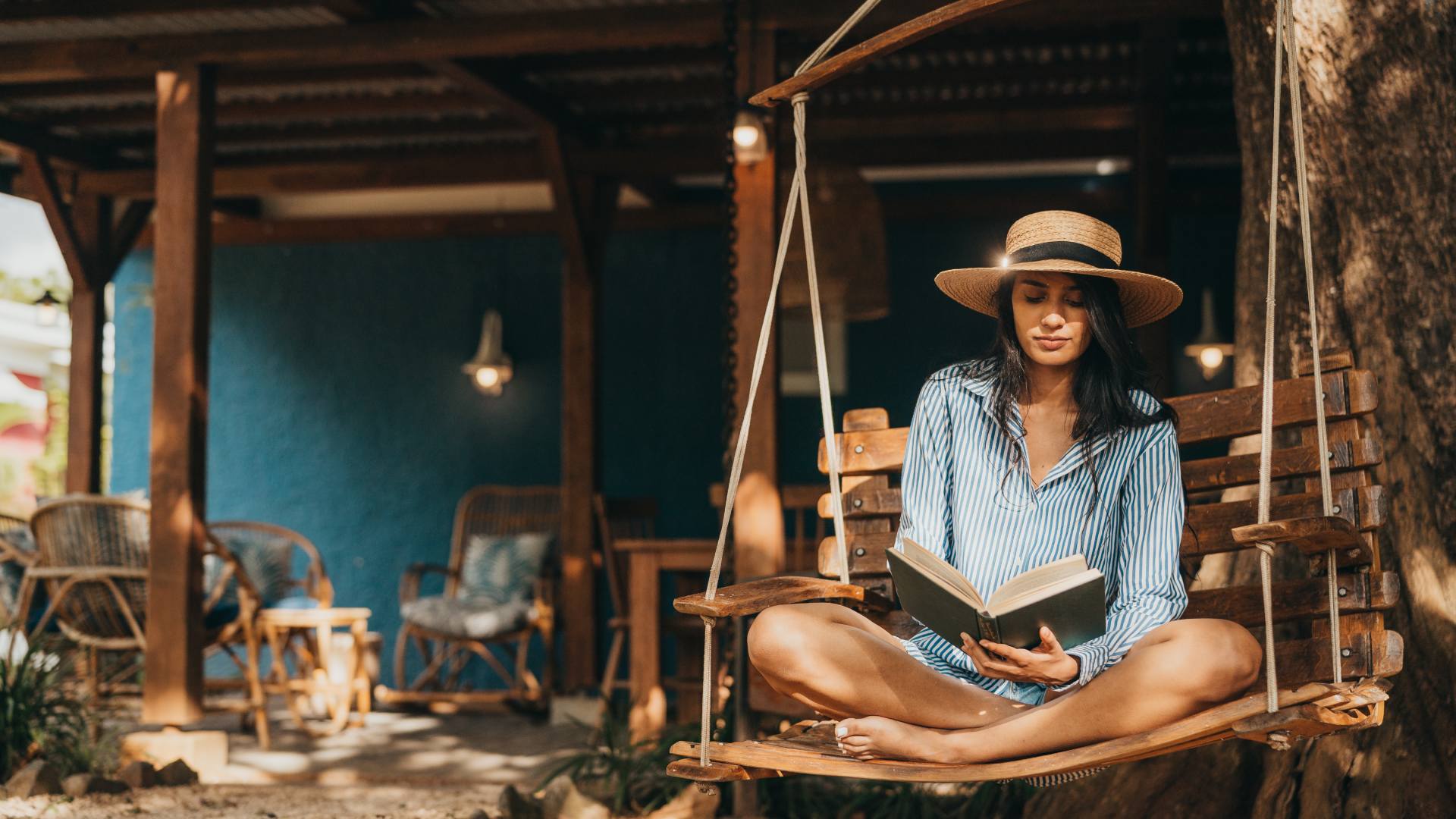 In Mauritius, a woman in a hat and blue shirt enjoys reading a book.